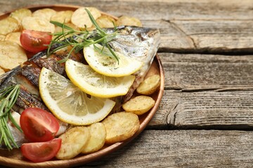 Tasty roasted dorado fish served with potatoes, tomatoes and lemon on wooden table, closeup and...