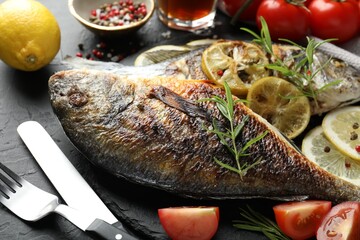 Tasty roasted dorado fish served on black table, closeup. Homemade seafood dish