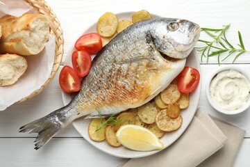 Tasty roasted dorado fish served with vegetables and sauce on white wooden table, flat lay. Homemade seafood dish