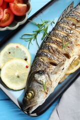 Tasty roasted seabass fish with spices and tomatoes on light blue wooden table, flat lay. Homemade seafood dish