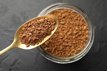 Spoon with granulated instant coffee and jar on dark textured table, top view