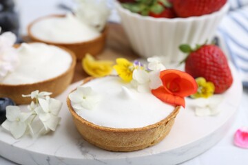 Delicious dessert. Tartlets with cream, berries and flowers on white tiled table, closeup