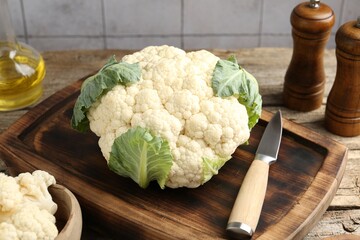Fresh cauliflower with green leaves, spices and knife on wooden table, closeup
