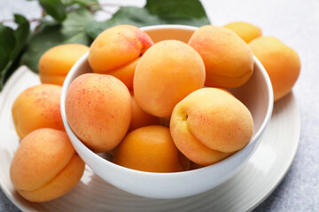 Fresh apricots in bowl on grey textured table, closeup