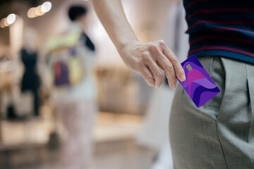 Woman pulls a credit card out of her trouser pocket while standing in front of a store in a shopping mall