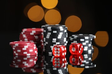 Casino chips and dice on mirror surface against blurred lights, closeup