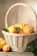Fresh apricots in wicker basket and green leaves on wooden table, closeup