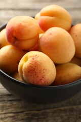 Fresh apricots in bowl on wooden table, closeup