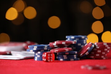 Casino chips, playing cards and die on red table against blurred lights, closeup