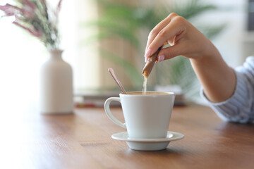 Woman hand throwing sugar in a coffee cup at home