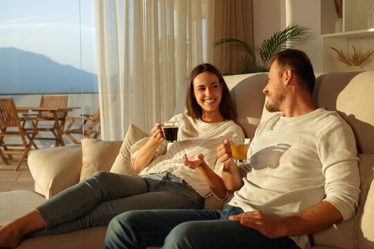 Happy couple talking drinking coffee and tea at home