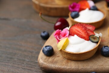 Sweet tartlets with berries and flowers on wooden table, closeup with space for text. Delicious dessert