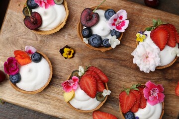 Sweet tartlets with berries and flowers on wooden table, top view. Delicious dessert