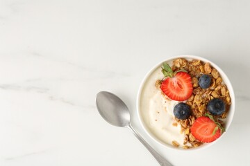 Tasty yogurt with granola, berries and spoon on white marble table, flat lay. Space for text
