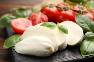 Tasty mozzarella cheese, tomatoes and basil on table, closeup