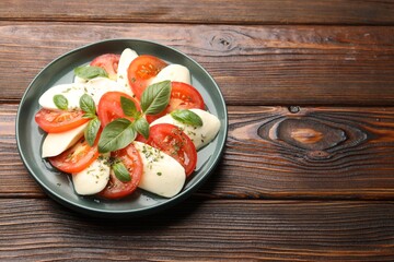 Tasty salad Caprese with mozzarella, tomatoes, basil and spices on wooden table. Space for text