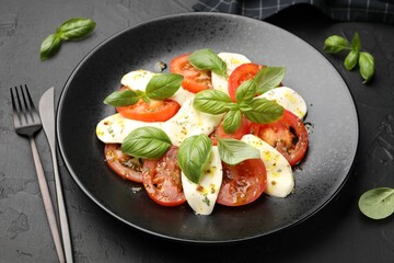 Tasty salad Caprese with mozzarella, tomatoes, basil and spices on black table, closeup