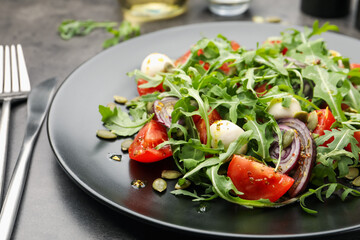 Tasty salad with arugula, mozzarella and vegetables served on grey table, closeup