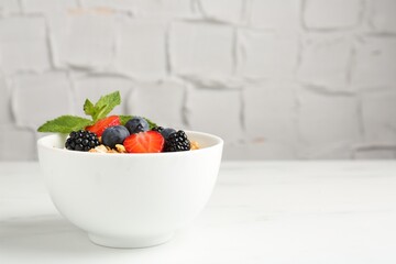 Tasty yogurt with granola and berries in bowl on white marble table, closeup. Space for text