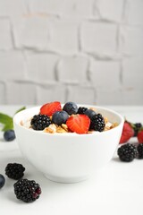 Tasty yogurt with granola and berries in bowl on white table, closeup. Space for text