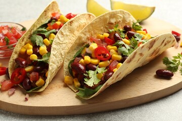 Tasty vegetarian tacos with beans, vegetables and lime on light grey table, closeup