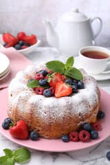 Tasty Bundt cake with powdered sugar and berries on white marble table, closeup