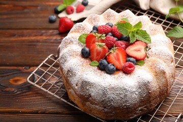 Tasty Bundt cake with powdered sugar and berries on wooden table, closeup. Space for text