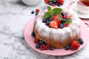 Tasty Bundt cake with powdered sugar and berries on white marble table, closeup. Space for text