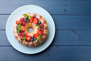 Delicious bundt cake with berries, glaze and mint on blue wooden table, top view. Space for text