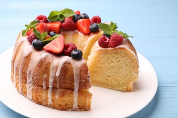 Pieces of delicious bundt cake with berries, glaze and mint on light blue wooden table, closeup