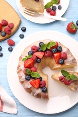 Pieces of delicious bundt cake with berries, glaze and mint served on light blue wooden table, flat lay