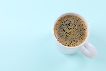 Aromatic coffee in cup on light turquoise background, above view. Space for text