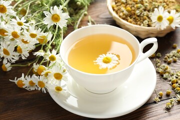 Tasty chamomile tea and flowers on wooden table, closeup