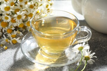 Tasty chamomile tea and flowers on light grey table, closeup