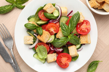 Delicious salad with croutons, vegetables and basil on wooden table, flat lay