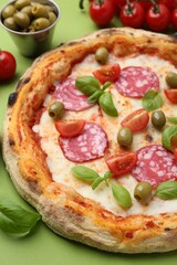 Delicious pizza with salami, olives, tomatoes and basil on green table, closeup