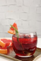 Tasty cocktail with grapefruit, ice cubes and rosemary on white table, closeup