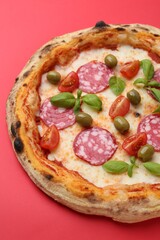Delicious pizza with salami, olives, tomatoes and basil on red table, closeup
