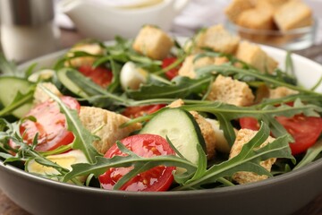Tasty salad with croutons, cucumbers, tomatoes and arugula on wooden table, closeup