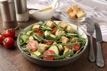 Tasty salad with croutons, cucumbers, tomatoes and arugula on wooden table, closeup