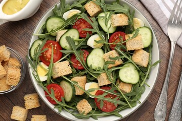 Tasty salad with croutons, cucumbers, tomatoes and arugula on wooden table, flat lay
