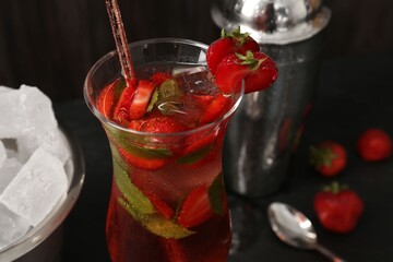 Refreshing strawberry cocktail in glass, metal shaker and ice in bucket on dark table, closeup