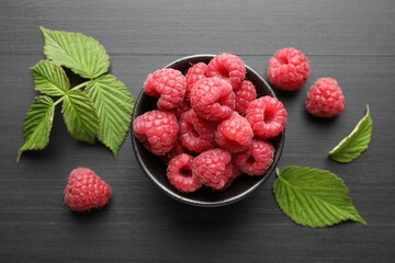 Tasty fresh ripe raspberries and leaves on black table, flat lay