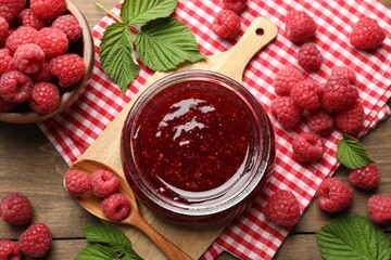 Tasty jam, fresh ripe raspberries and leaves on wooden table, flat lay