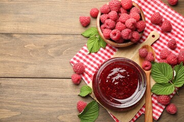 Tasty jam, fresh ripe raspberries and leaves on wooden table, flat lay. Space for text