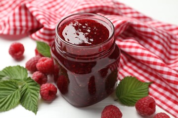 Tasty jam, fresh ripe raspberries and leaves on white wooden table, closeup