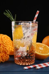 Sparkling water with orange in glass, fresh fruits and straws on blue wooden table, closeup