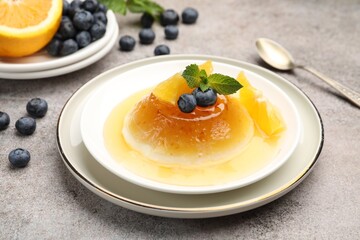 Tasty panna cotta with orange, blueberries and mint on light grey table, closeup