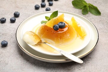 Tasty panna cotta with orange, blueberries and mint on light grey table, closeup