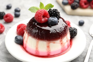 Tasty panna cotta with berries and jam on light grey table, closeup